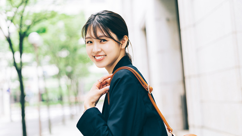 肩にベージュのバッグを掛けて振り返る黒髪の女性