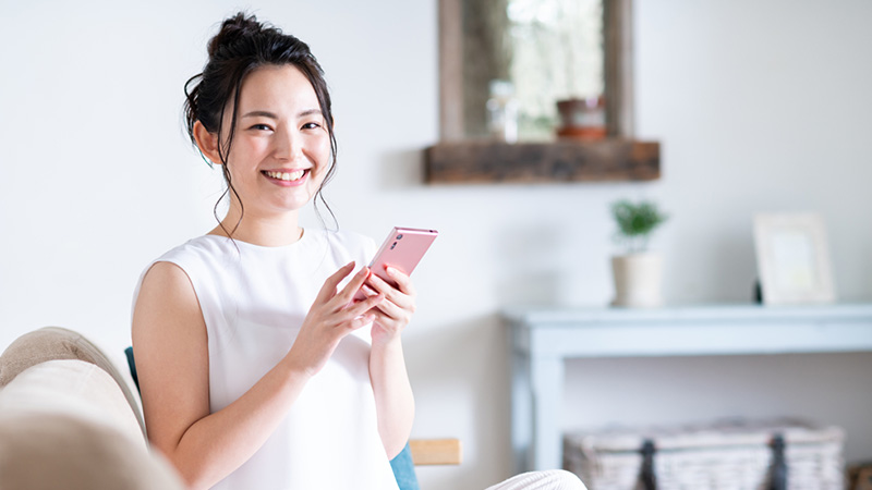 ソファに座りスマホを操作しながら笑顔を見せる女性