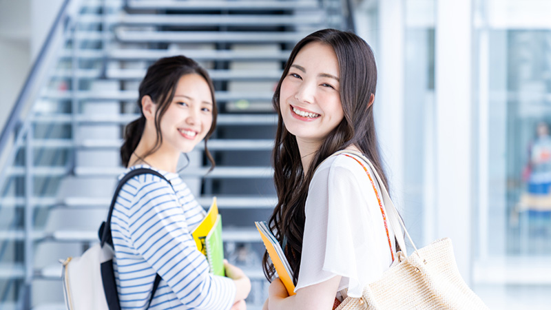 本やノートを抱えて笑顔で振り返る2人の女性