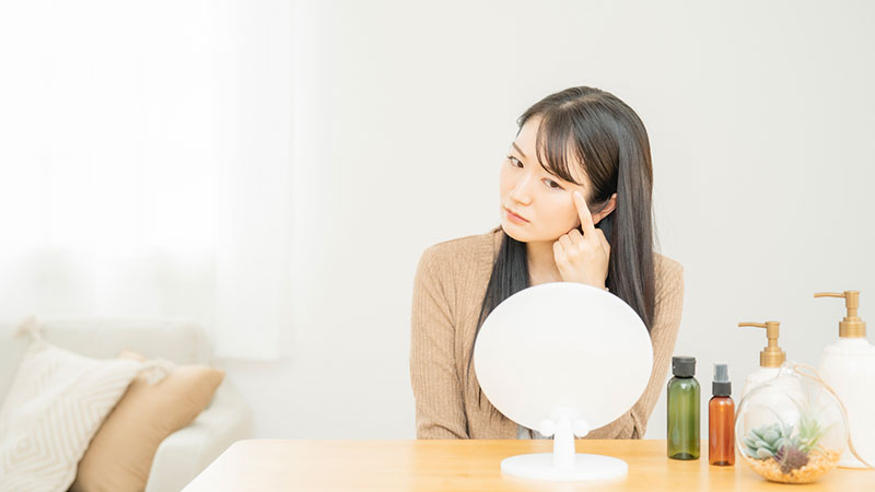 鏡で目を見ながら悩む女性