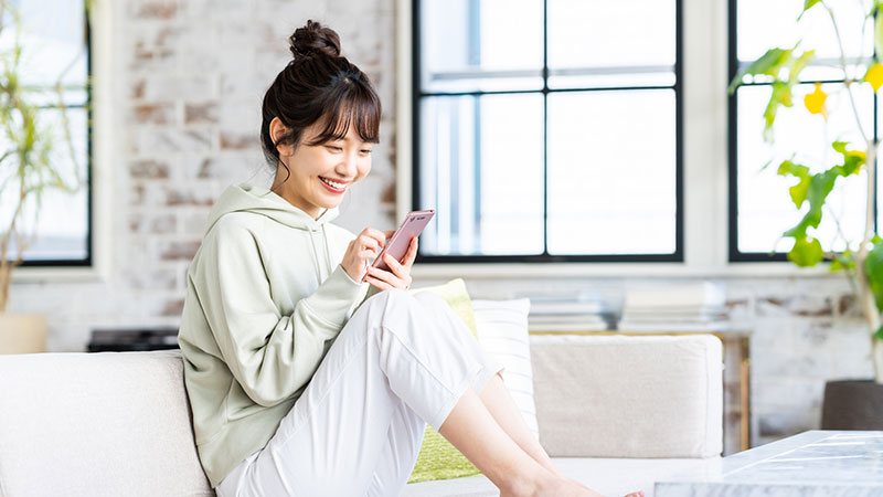 ソファの上でスマホを見てほほ笑む女性